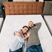 overhead view of smiling couple lying on bed in furniture store with arranged mattresses